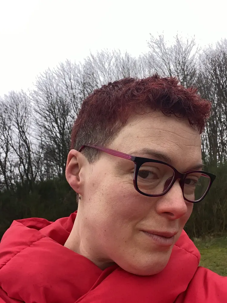 Woman with a cropped red-toned haircut, tapered at the sides