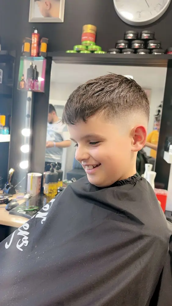 Boy having his hair cut in front of the mirror, shelves of styling products behind